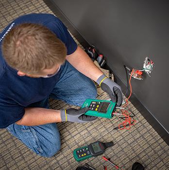 McElroy Electric electrician tests the wiring behind a wall outlet.